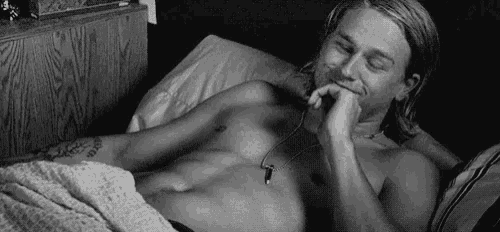 a shirtless man is laying on a bed with his hand on his chin .