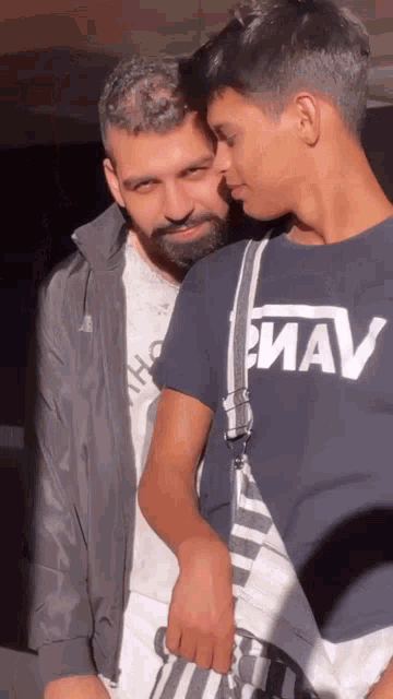 a man with a beard is hugging another man with a shirt that says mav