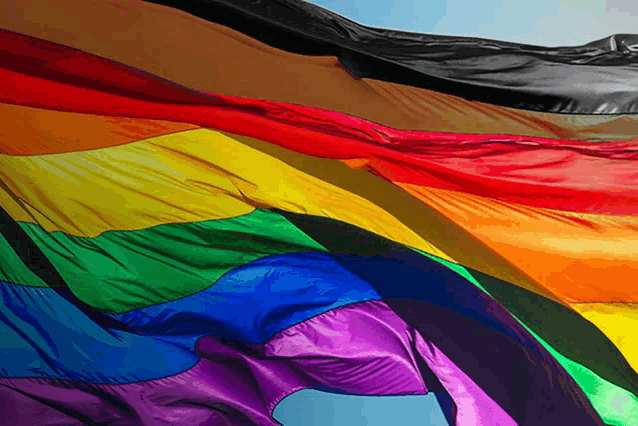 a rainbow flag is waving in the wind along with a black flag