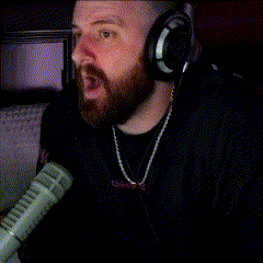 a man with a beard wearing headphones and a chain around his neck is singing into a microphone ..