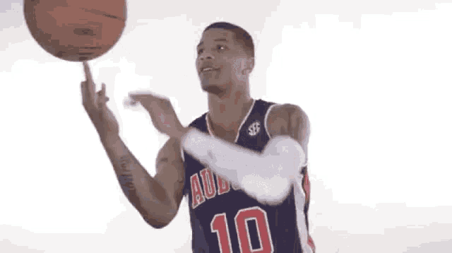 a basketball player wearing a blue jersey with the number 10 on it is spinning a basketball on his finger .