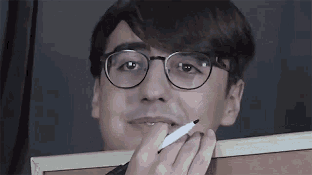 a man wearing glasses is holding a marker to his mouth .