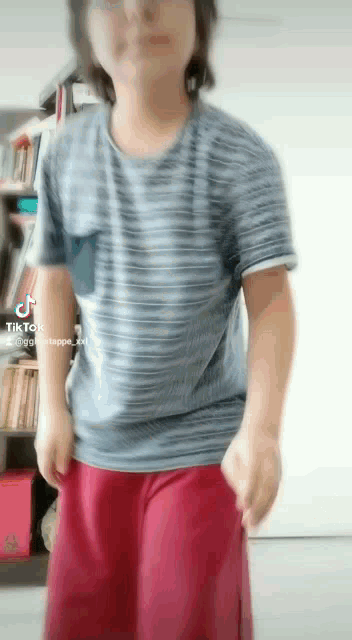 a man wearing a striped shirt and red shorts is standing in front of a bookshelf ..