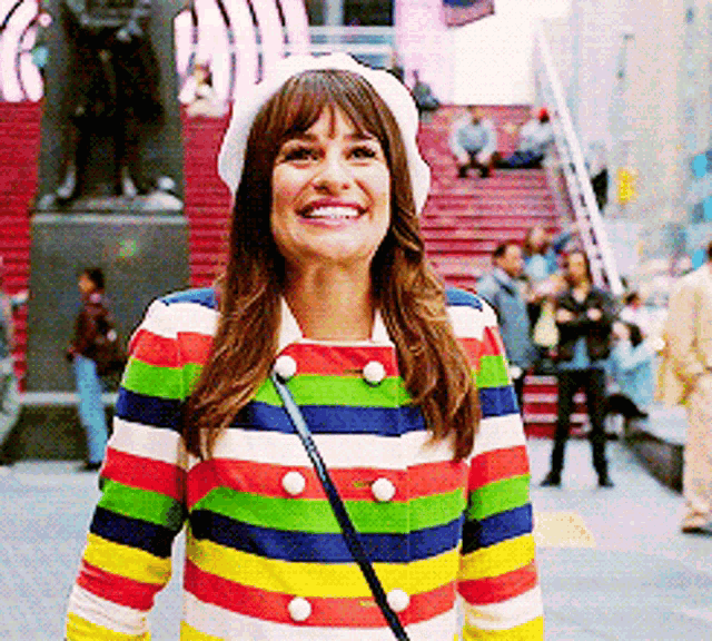 a woman wearing a striped jacket and a white hat smiles for the camera