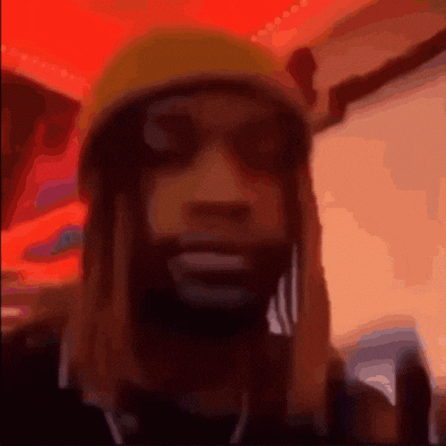 a man with long hair and a beard is wearing a yellow hat and sunglasses and giving the middle finger .