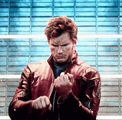 a man in a red leather jacket is standing in front of a blue wall and making a funny face .