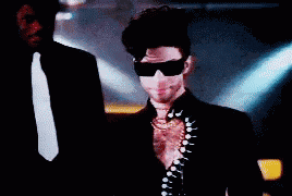a man in a suit and tie adjusts his sunglasses while another man stands behind him