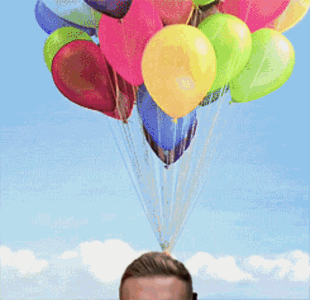 a bunch of colorful balloons are hanging from a string over a man 's head