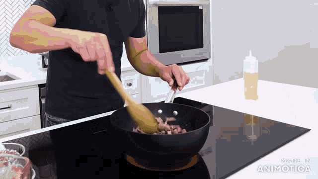 a man stirs food in a frying pan with a wooden spoon while a bottle of sauce sits on a counter