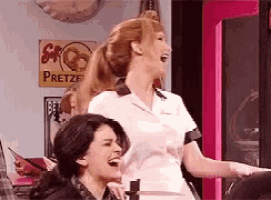 two women are laughing in front of a pretzel sign