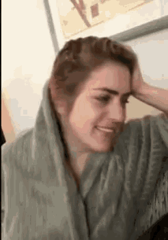 a woman is holding her head and smiling while wearing a scarf around her neck .