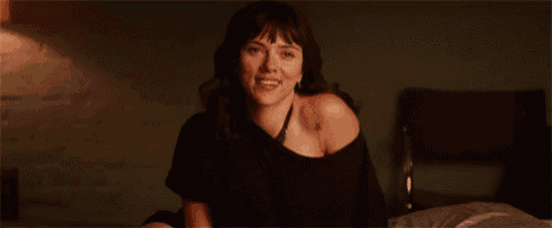a woman is sitting on a bed wearing a black shirt and smiling .