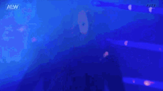 a man in a black jacket is standing in a dark room with a blue background .
