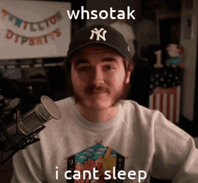 a man wearing a ny yankees hat is sitting in front of a microphone