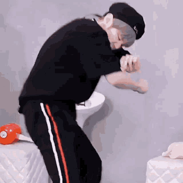 a man wearing a black hat and black pants is dancing in a bathroom .