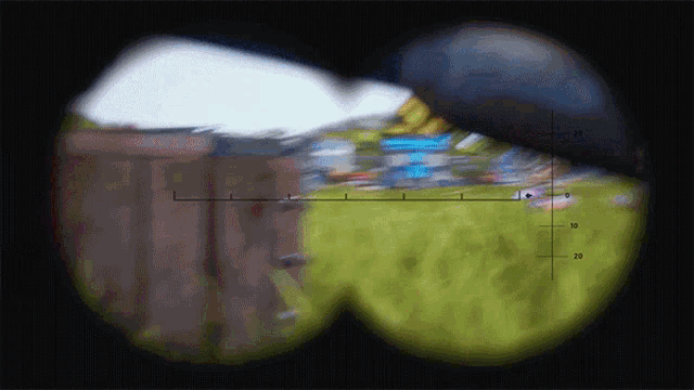 a sniper scope shows a field of grass and trees with a few buildings in the distance