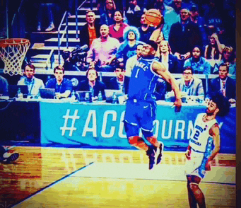 a basketball player is jumping in the air while another player looks on