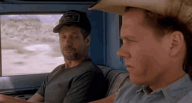 two men are sitting in a car and one of them is wearing a hat that says alliance