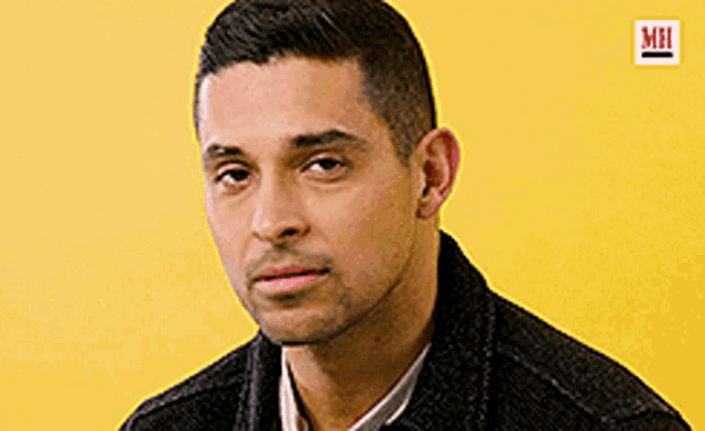a man wearing a black jacket and a white shirt is looking at the camera on a yellow background .