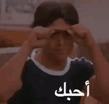 a young man is making a funny face with his hands in front of his face and the words `` i love you '' in arabic .