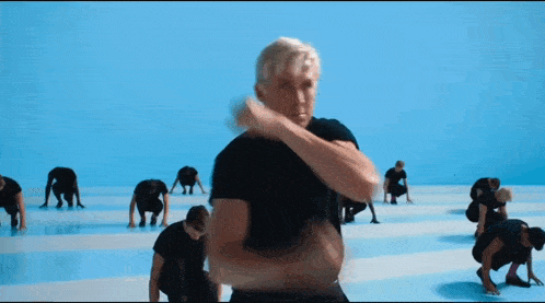 a man in a black shirt stands in front of a group of people doing exercises