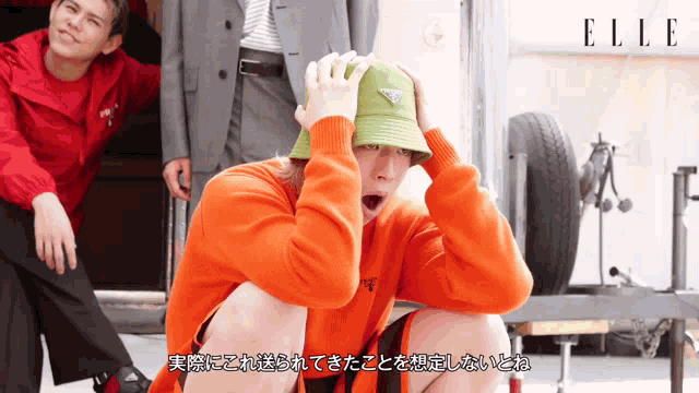 a man wearing an orange sweater and a green hat with prada written on it
