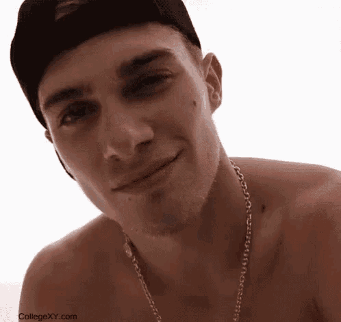 a shirtless man wearing a baseball cap and a chain around his neck is smiling .