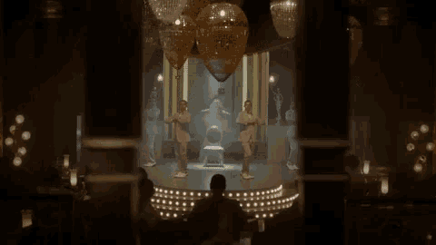 a group of people are dancing on a stage in a dark room in front of a crowd of people .