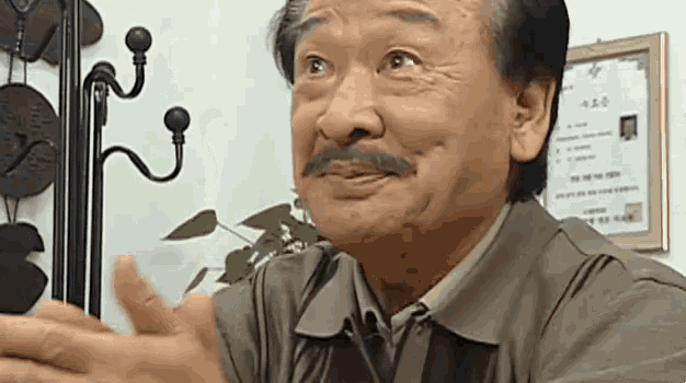 a man with a mustache is sitting at a table with his hands outstretched and making a funny face .