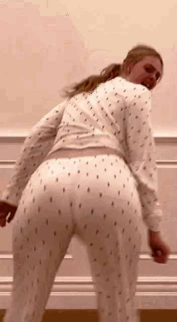 a woman in white pajamas is dancing in front of a white wall .