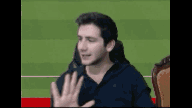a man is sitting in a chair with his hands up in front of a green field .