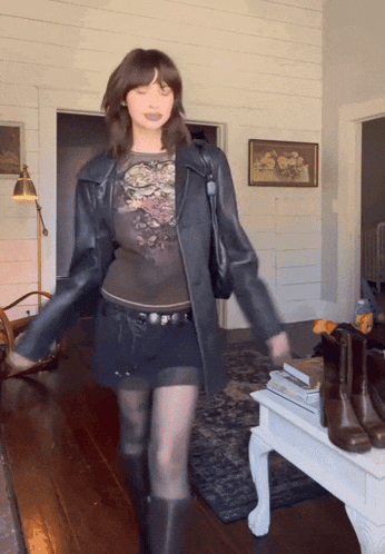 a woman wearing a black leather jacket and a black skirt is standing in a living room
