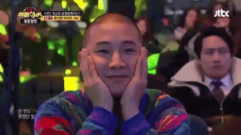 a man with a shaved head is sitting in front of a jtbc sign