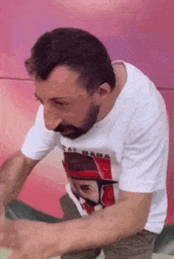 a man with a beard is wearing a white t-shirt with a picture of a man in a hat .
