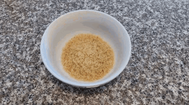 a white bowl filled with brown rice is sitting on a marble counter .