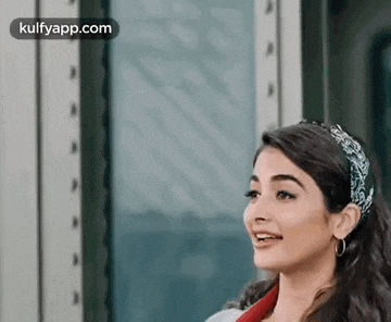 a woman wearing a headband and earrings is standing in front of a window and smiling .