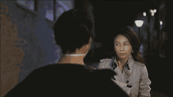 a woman in a trench coat is talking to another woman in a black dress