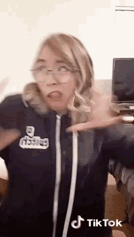 a woman wearing glasses is making a funny face in front of a tv with a tiktok logo on the bottom