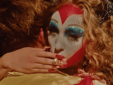 a woman with a red heart painted on her face holds a cigarette in her mouth