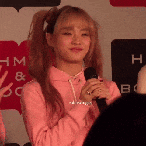 a girl in a pink sweatshirt is holding a microphone in front of a sign that says hm