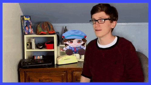 a boy wearing glasses stands in front of a stuffed toy of a boy in a blue hat