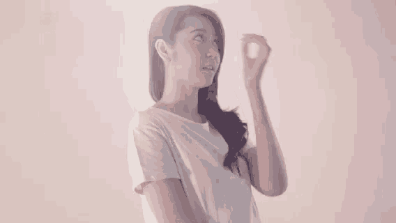 a woman in a white shirt is standing in front of a pink wall and touching her forehead .