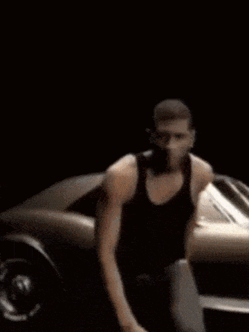 a man in a black tank top is kneeling down in front of a car .