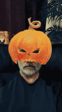 a man wearing a pumpkin mask is sitting in front of a sign that says ' aah ' on it