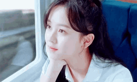 a young woman is sitting on a train and looking out the window .