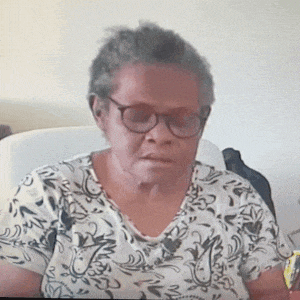 an older woman wearing glasses and a floral shirt is sitting on a couch