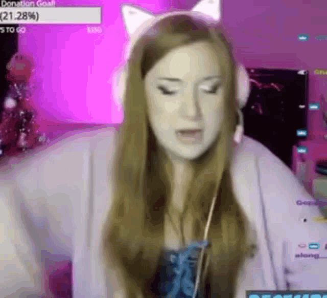 a woman wearing headphones and a cat ear headband is sitting in front of a computer screen .