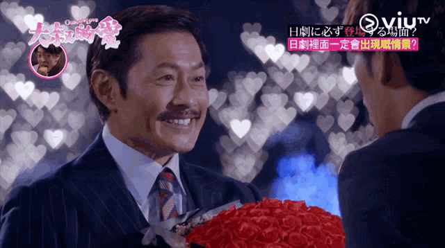 a man in a suit and tie is holding a bouquet of red roses and smiling
