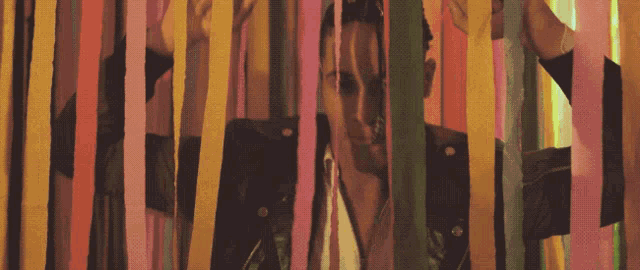 a man in a leather jacket behind a colorful striped wall