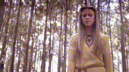 a woman with long blonde hair is standing in a forest